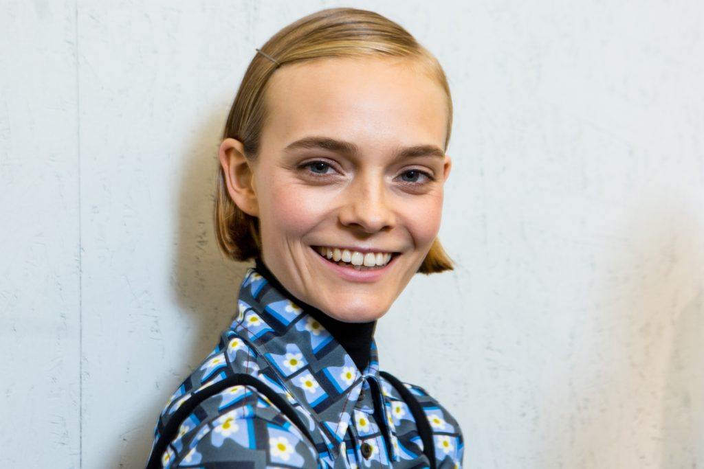 model with blonde bob hair tucked behind her ears, wearing a blue outfit and smiling