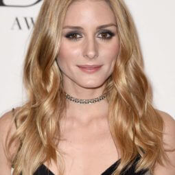 Oilia Palermo with a honey blonde wavy hair on the red carpet wearing a black dress and a jewelled necklace