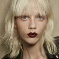 model with platinum blonde hair cut into a short shag haircut and blunt bangs, wearing dark red lipstick