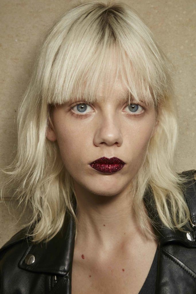 model with platinum blonde hair cut into a short shag haircut and blunt bangs, wearing dark red lipstick
