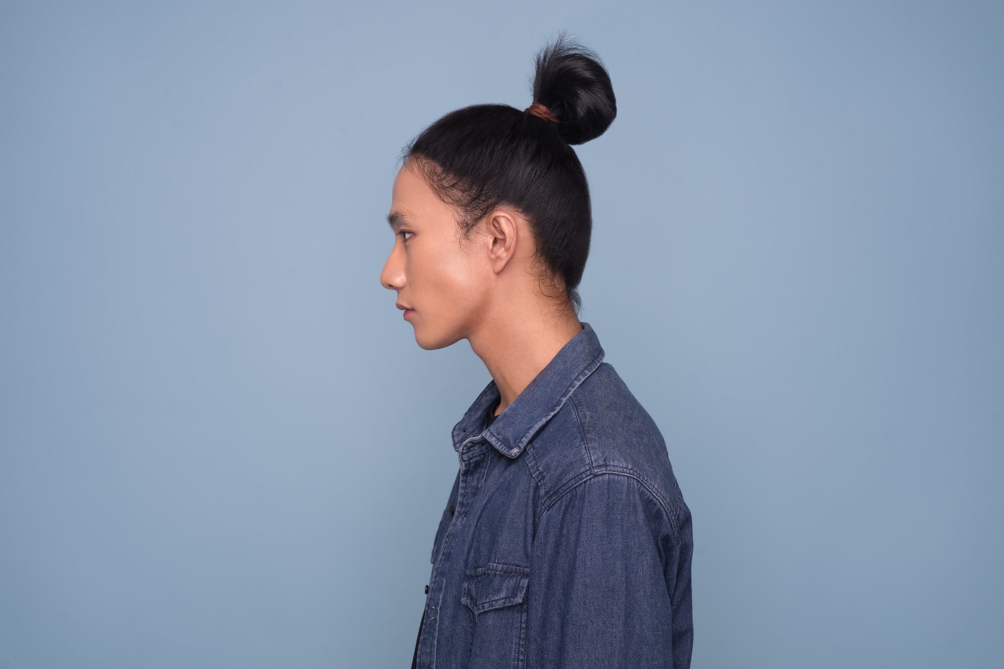 Asian men hairstyles: A young Asian man with shoulder-length straight hair in a man bun