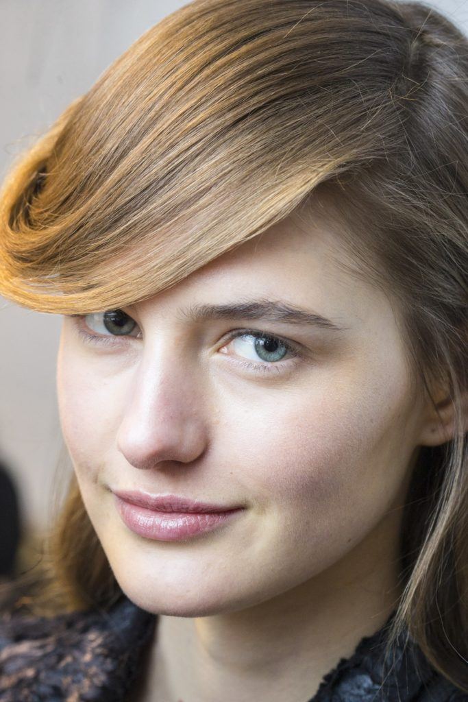 model with brown-blonde hair styled into a deep side parting and large sweeping bangs