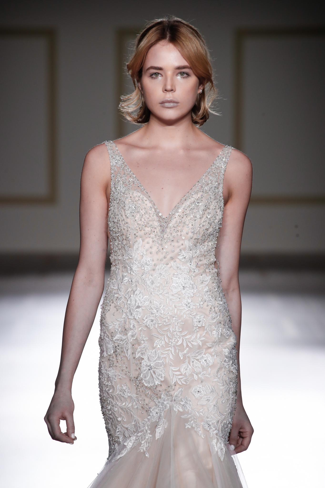 Wedding hairstyles for short hair: Woman with short blonde hair in a half-up half-down with Bardot fringe wearing a wedding dress on runway.