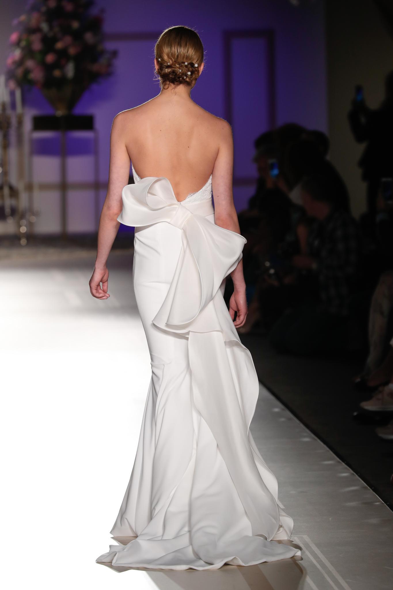Wedding hairstyles for short hair: Woman with short dark blonde hair in low updo with pearl hair accessories wearing a wedding dress on the runway.