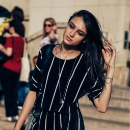 bruentte street styler with glossy hair swept to one side wearing an all in one stripe jumpsuit