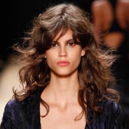 Medium length hairstyles for fine hair: Woman with brown medium length hair with messy waves and side fringe on runway.
