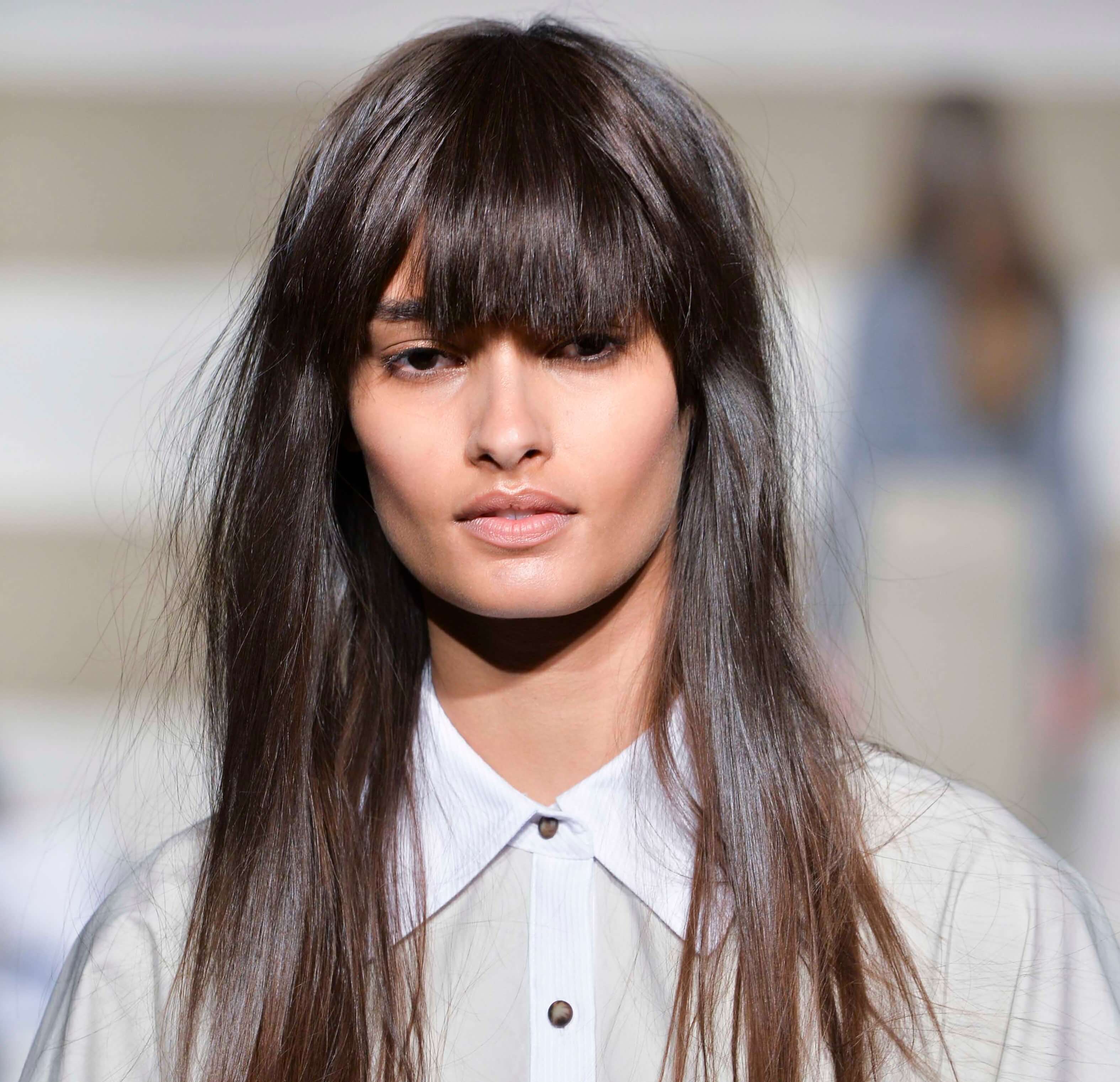 woman on the runway with long dark brown hair worn straight and with a full fringe cut in
