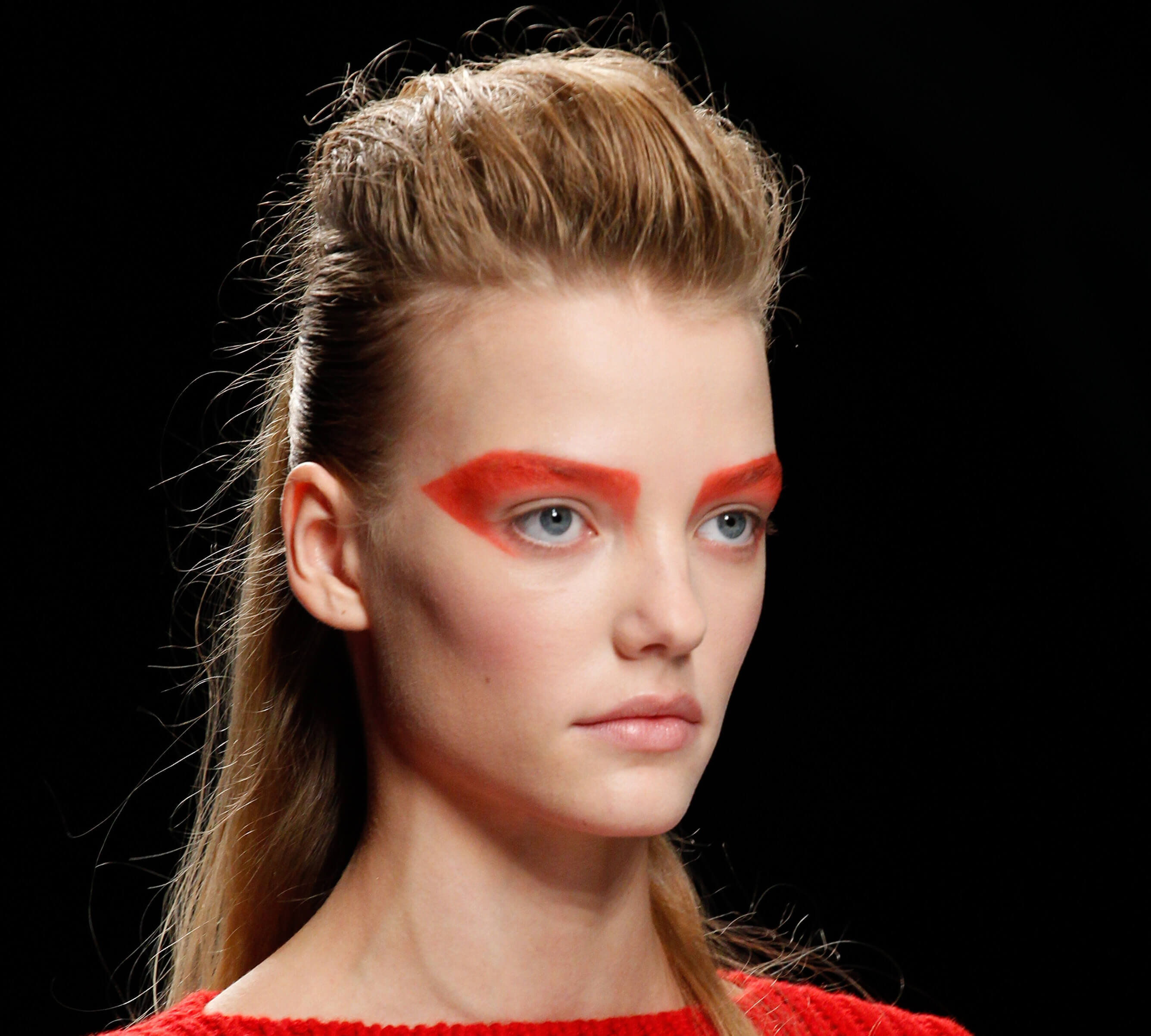 Medium length hairstyles for fine hair: Woman with blonde straight hair styled in a ponytail with a retro quiff with bold red eyeshadow on runway.