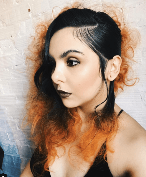side view of a woman with dark slicked back hair and orange coloured ends of her hair