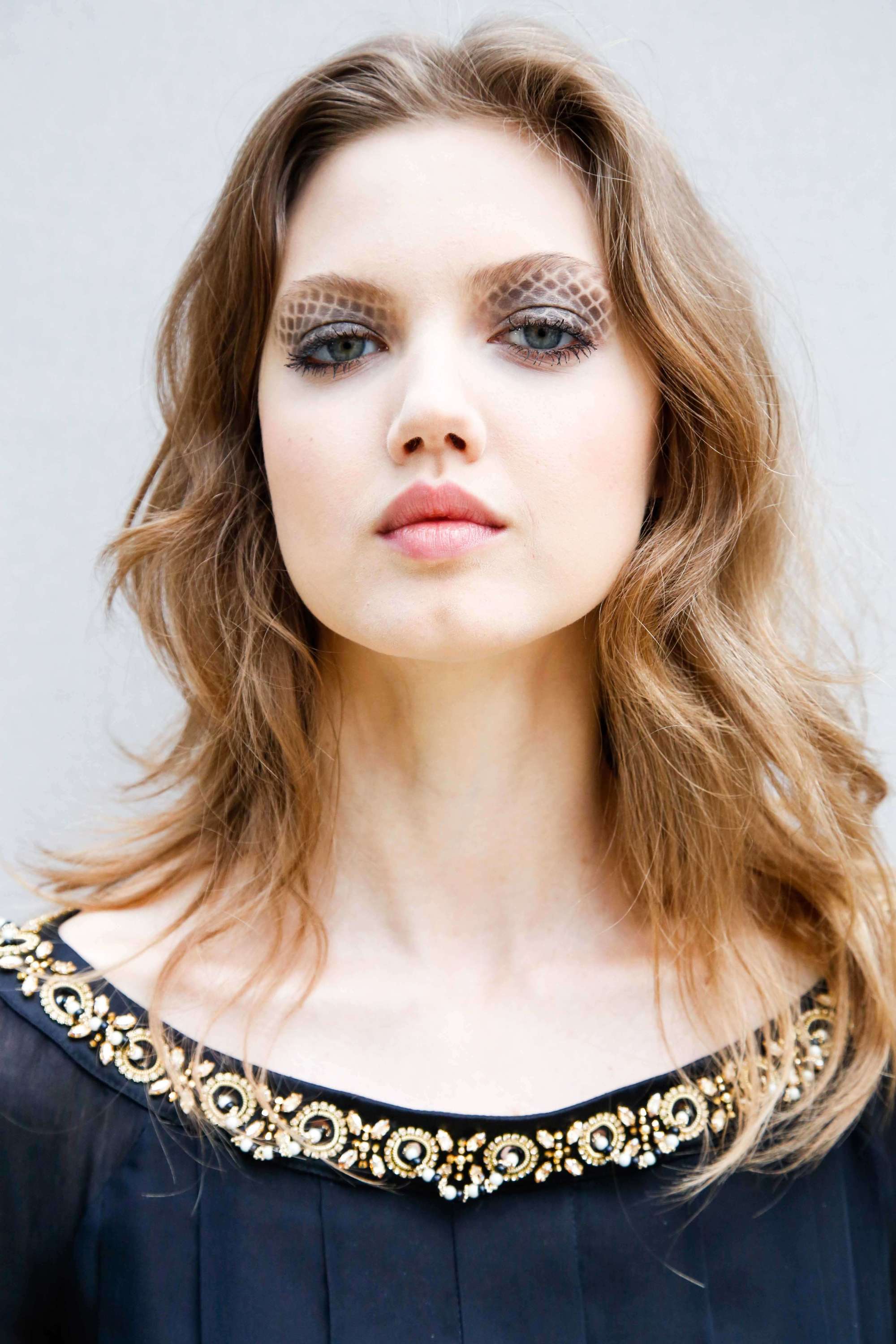 Haircuts for thick hair: Close up headshot of a model with light brown wavy hair worn in a shaggy mid-length cut.