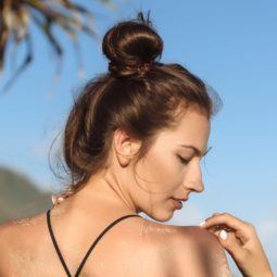 summer hair tips: close up shot of woman on the beach with dark brown hair fashioned into a bun, wearing a bikini top and posing
