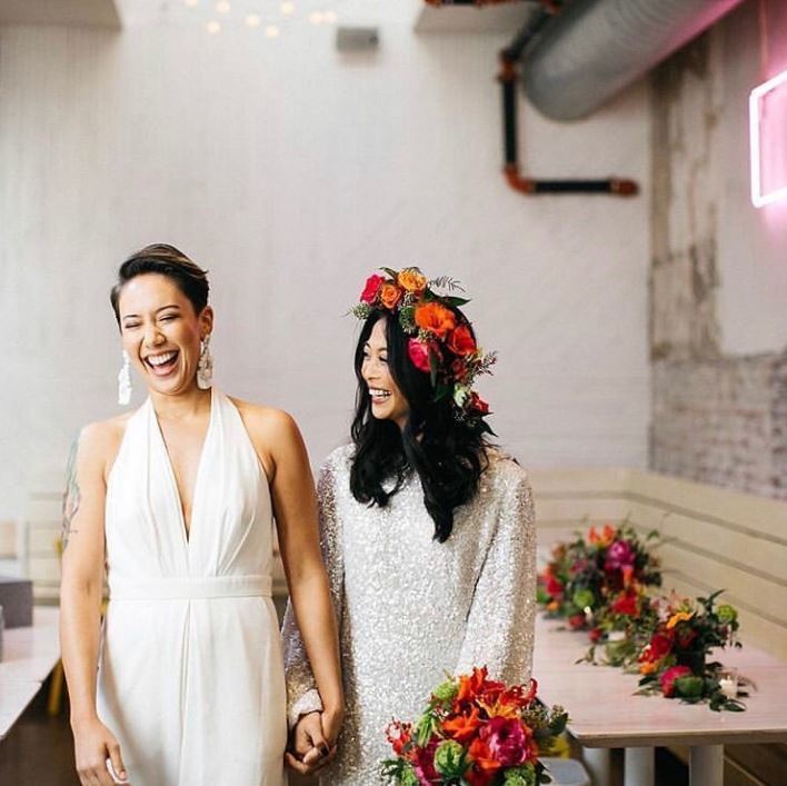 Wedding hairstyles for short hair: Two women wearing wedding outfits holding hands laughing.