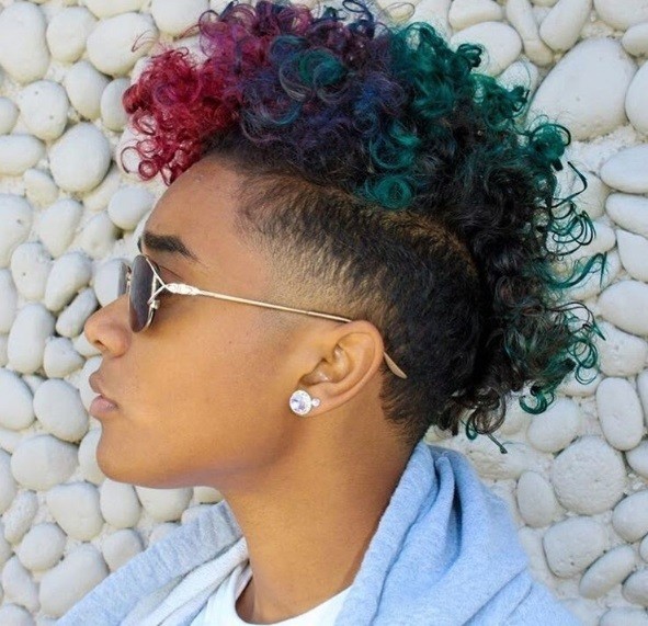 close up shot of woman with a watermelon dyed curly mohawk, wearing sunglasses, a blue top and posing outside