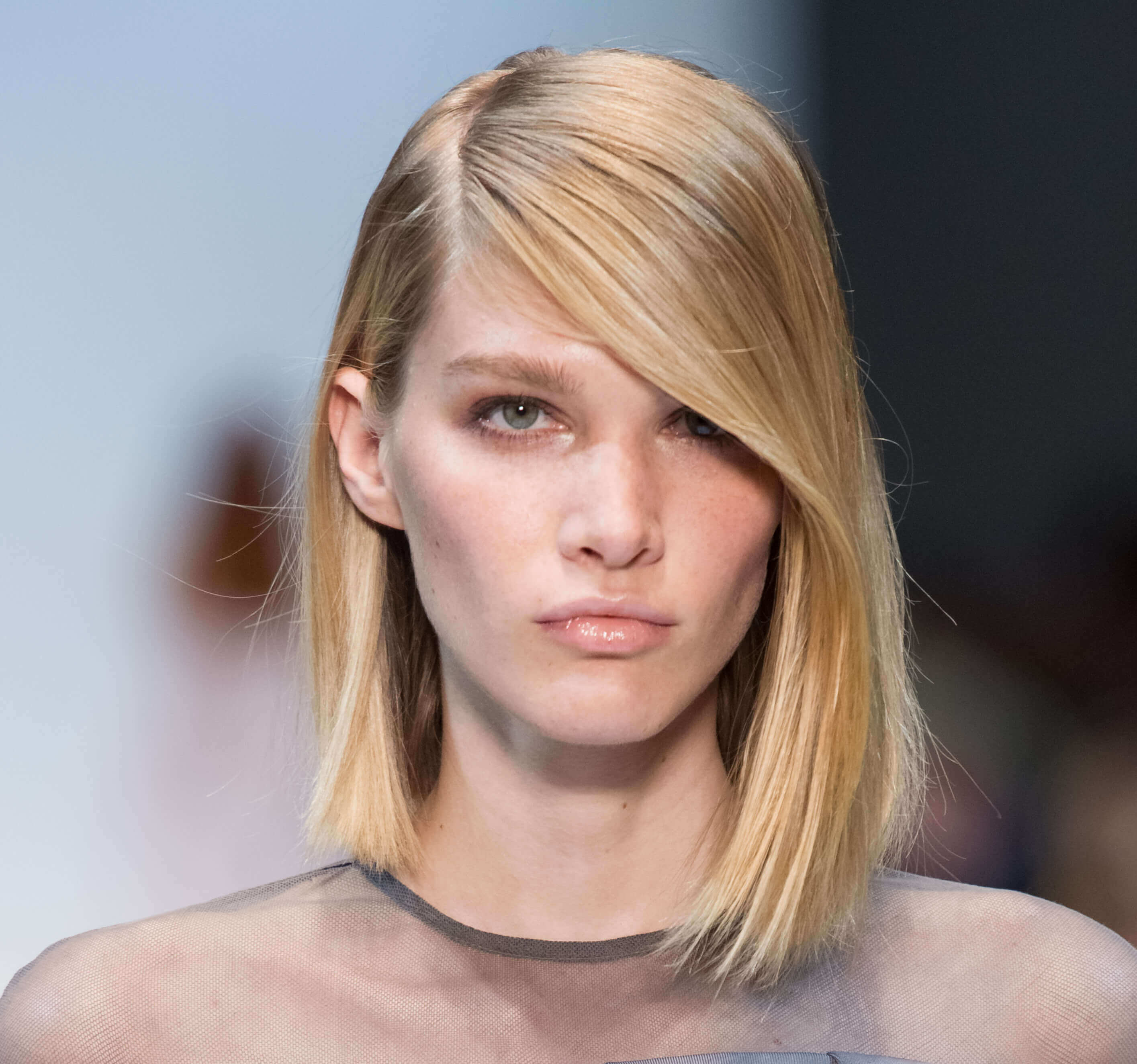 Short hairstyles for fine hair: Model in runway with asymmetrical blonde bob with deep side parting.