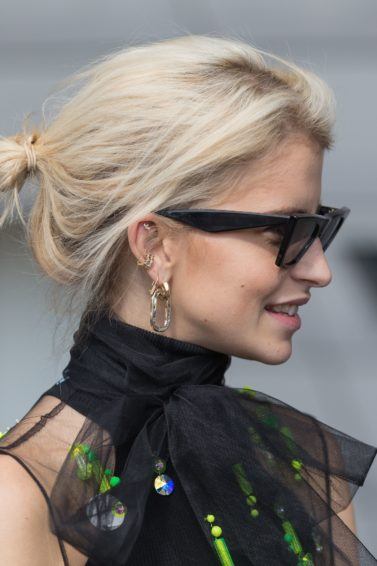 Best shampoo for fine hair: Caroline Daur with her short, bleach blonde fine hair styled into a messy bun updo, wearing sunglasses with black dress on the street
