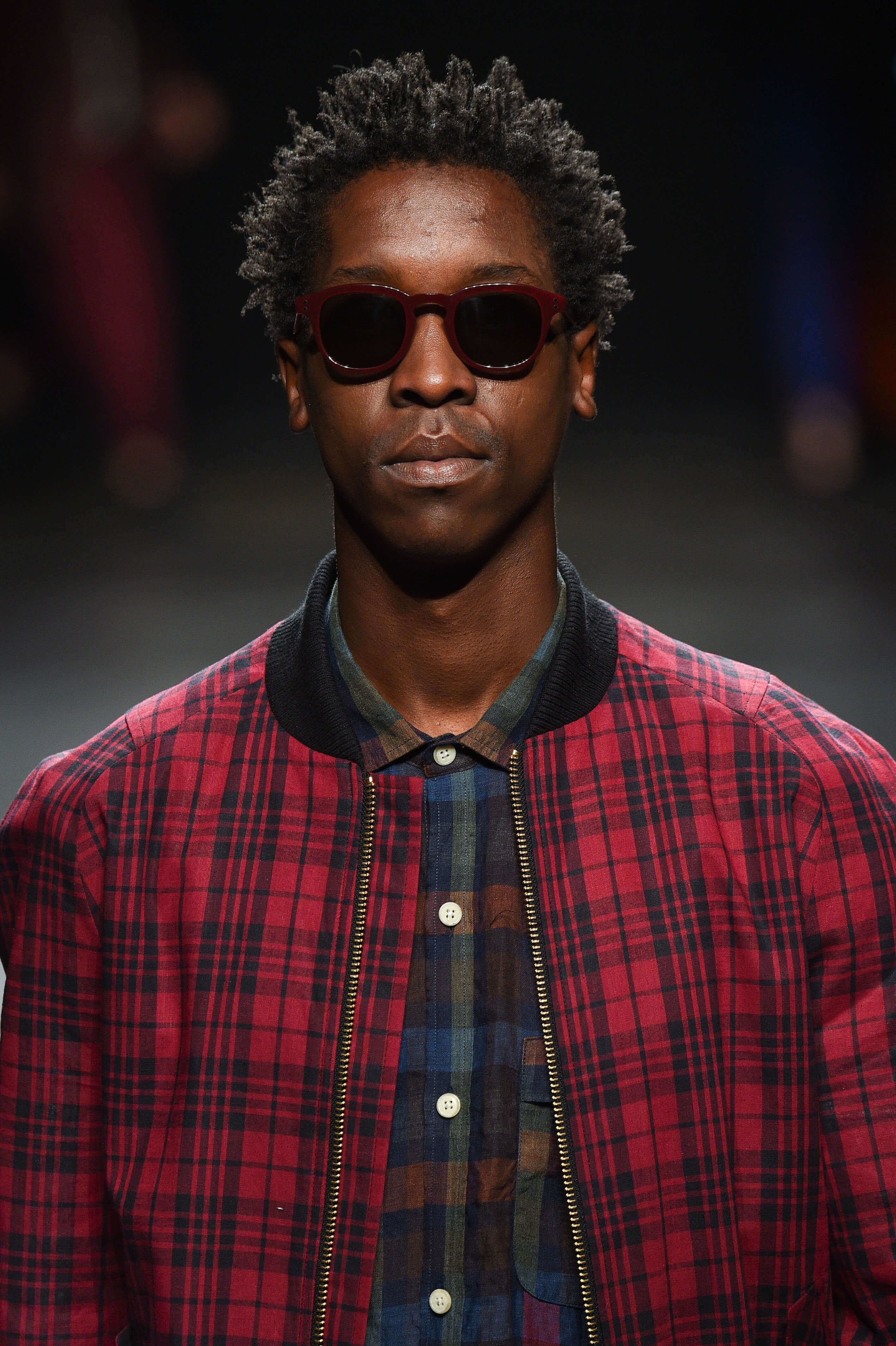 close up shot of man with mini twisted afro, wearing red jacket and checked top on the runway