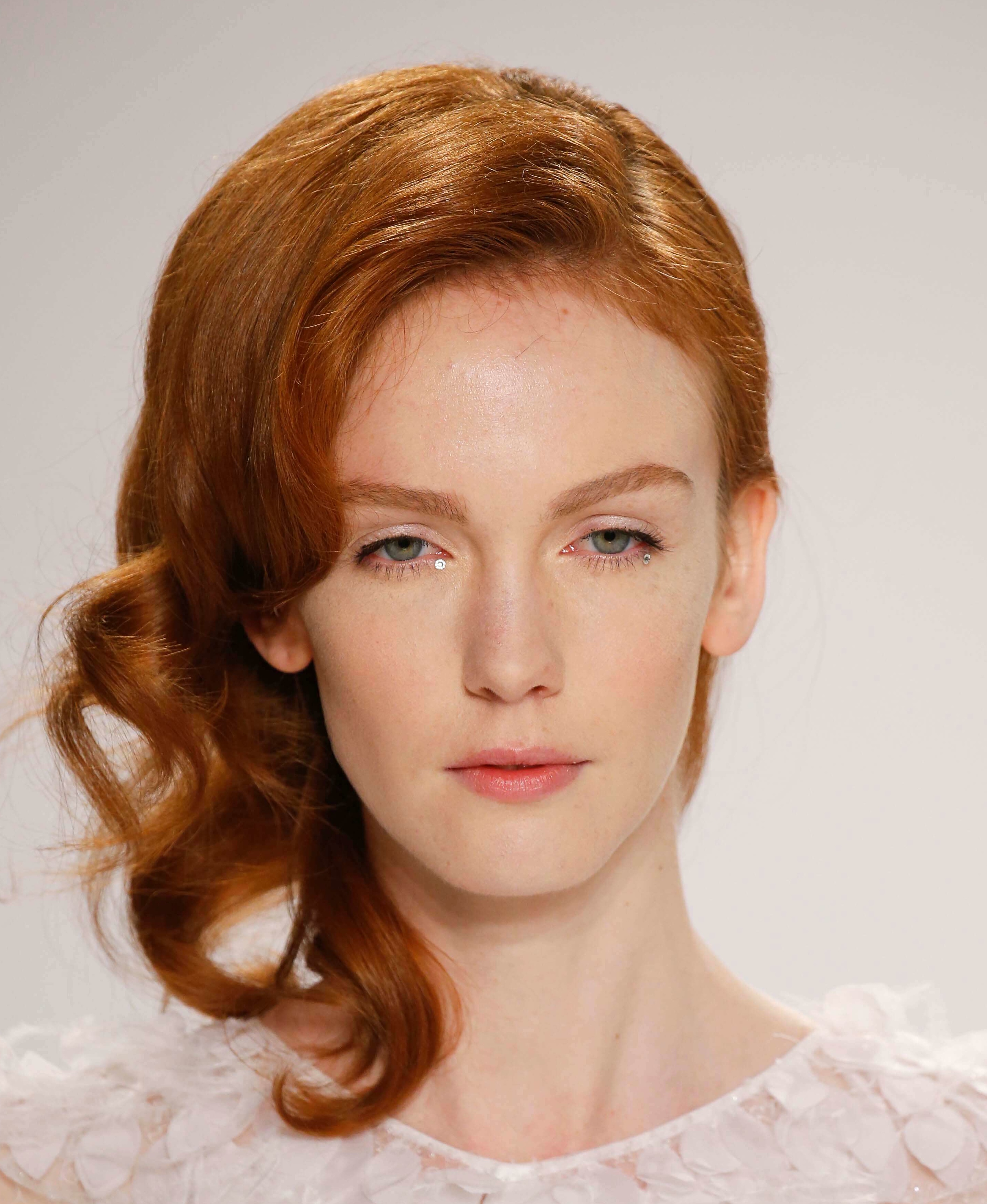 Prom hairstyles: Woman with red hair in side swept curls wearing a white top on runway.