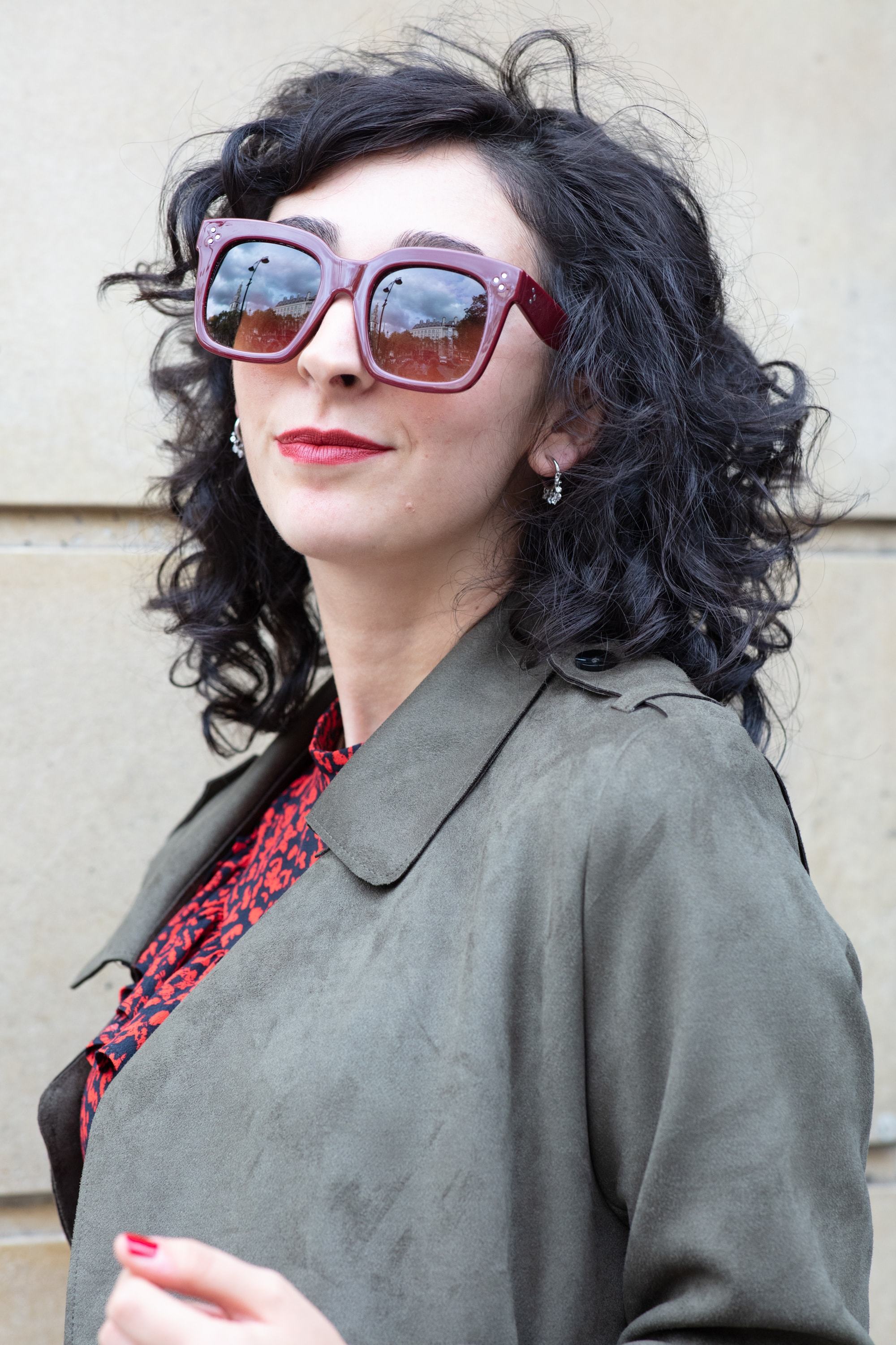 Woman with dark brown medium-length tight curls, wearing a grey jacket and red top on the street