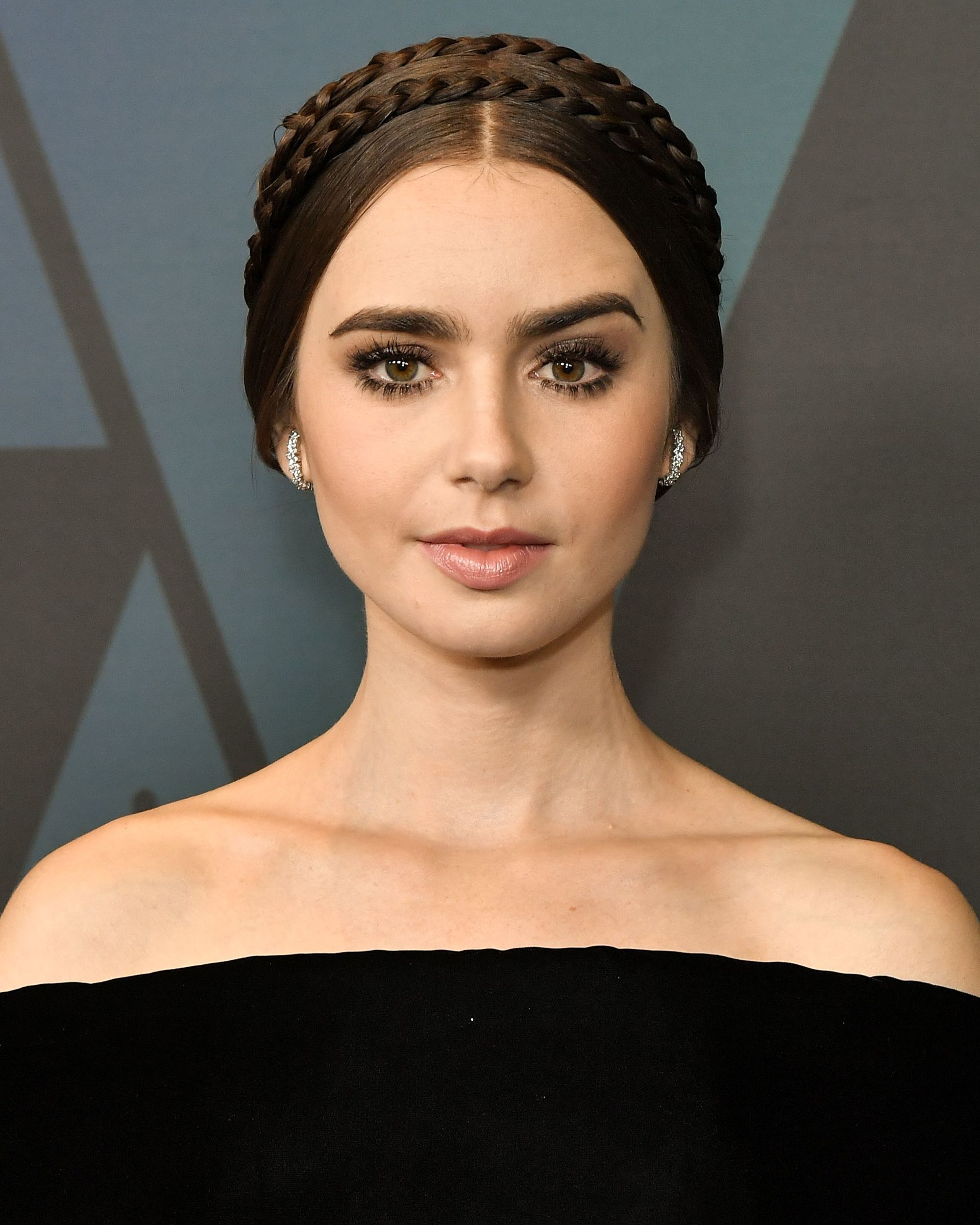 Lily Collins with dark brown hair styled into a double milkmaid braid, wearing a black dress on the red carpet
