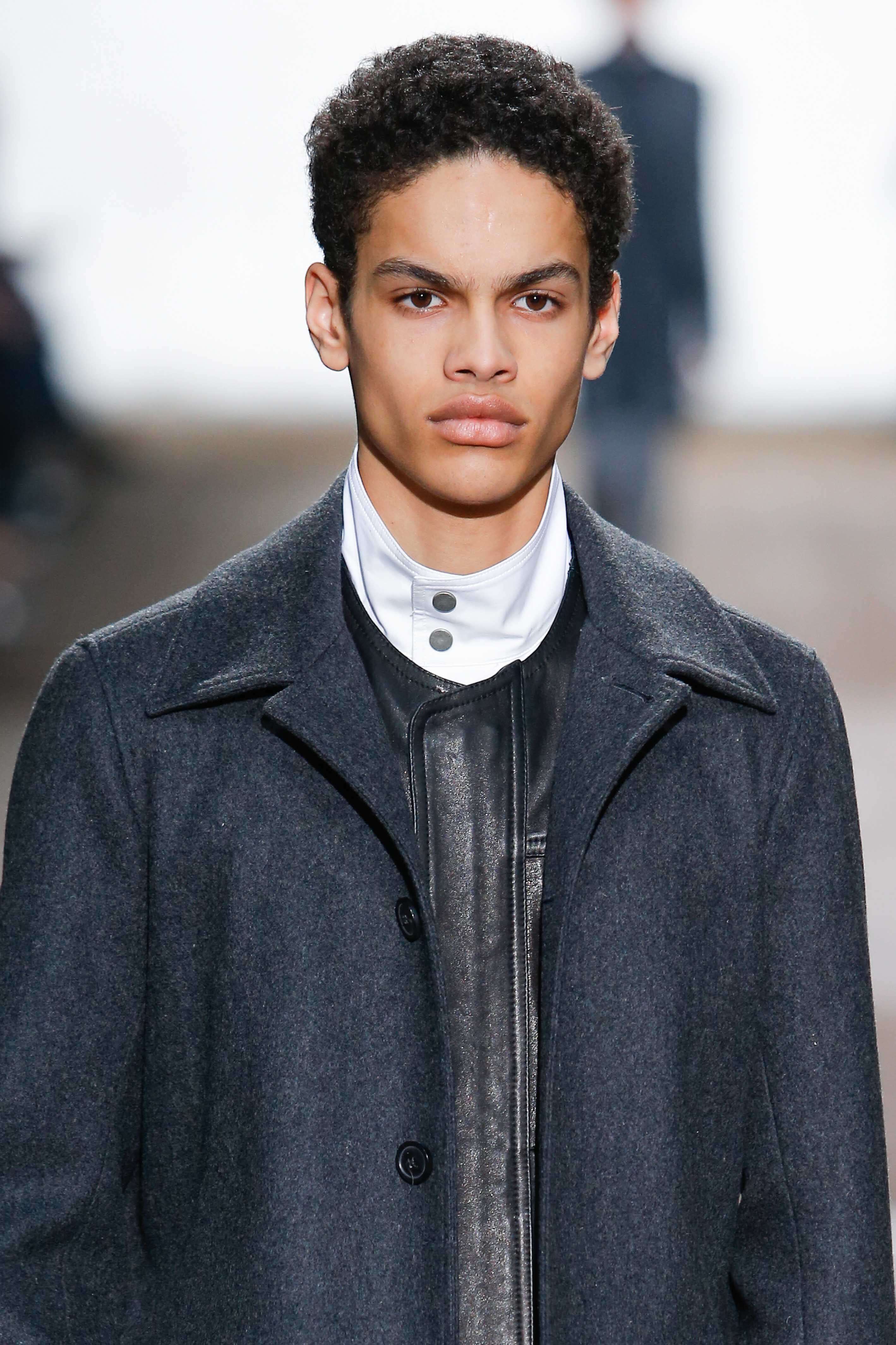 close up shot of a male model with mini afro hairstyle, wearing jacket on the runway