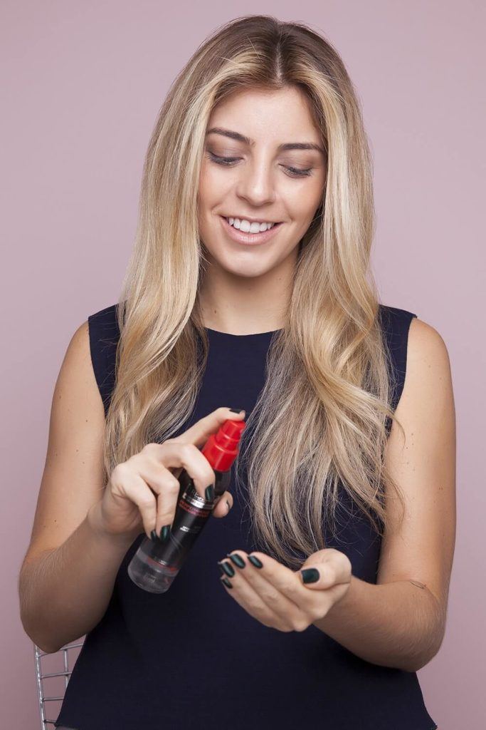 a blonde woman applying hairspray on the hand