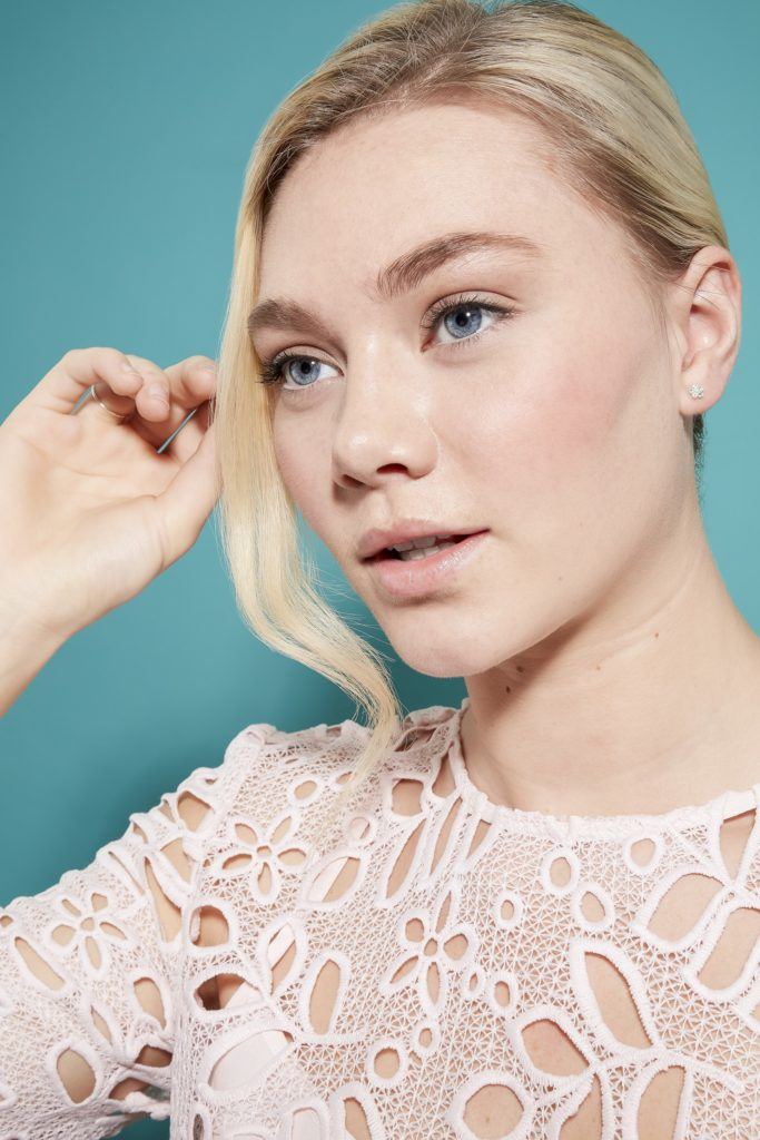 model with light blonde hair rolled into a french twist updo, pulling hair out from the front of her look to frame here face