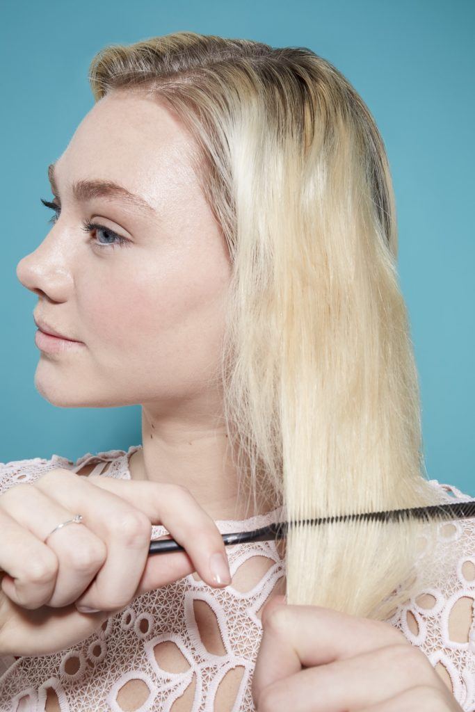 model with light blonde hair and darker roots using a comb to create volume in her hair