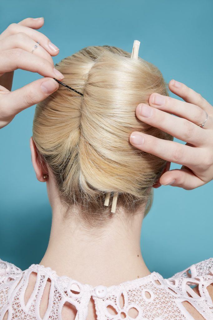 model with light blonde hair rolled into a french twist updo, pinning it in place with a bobby pin