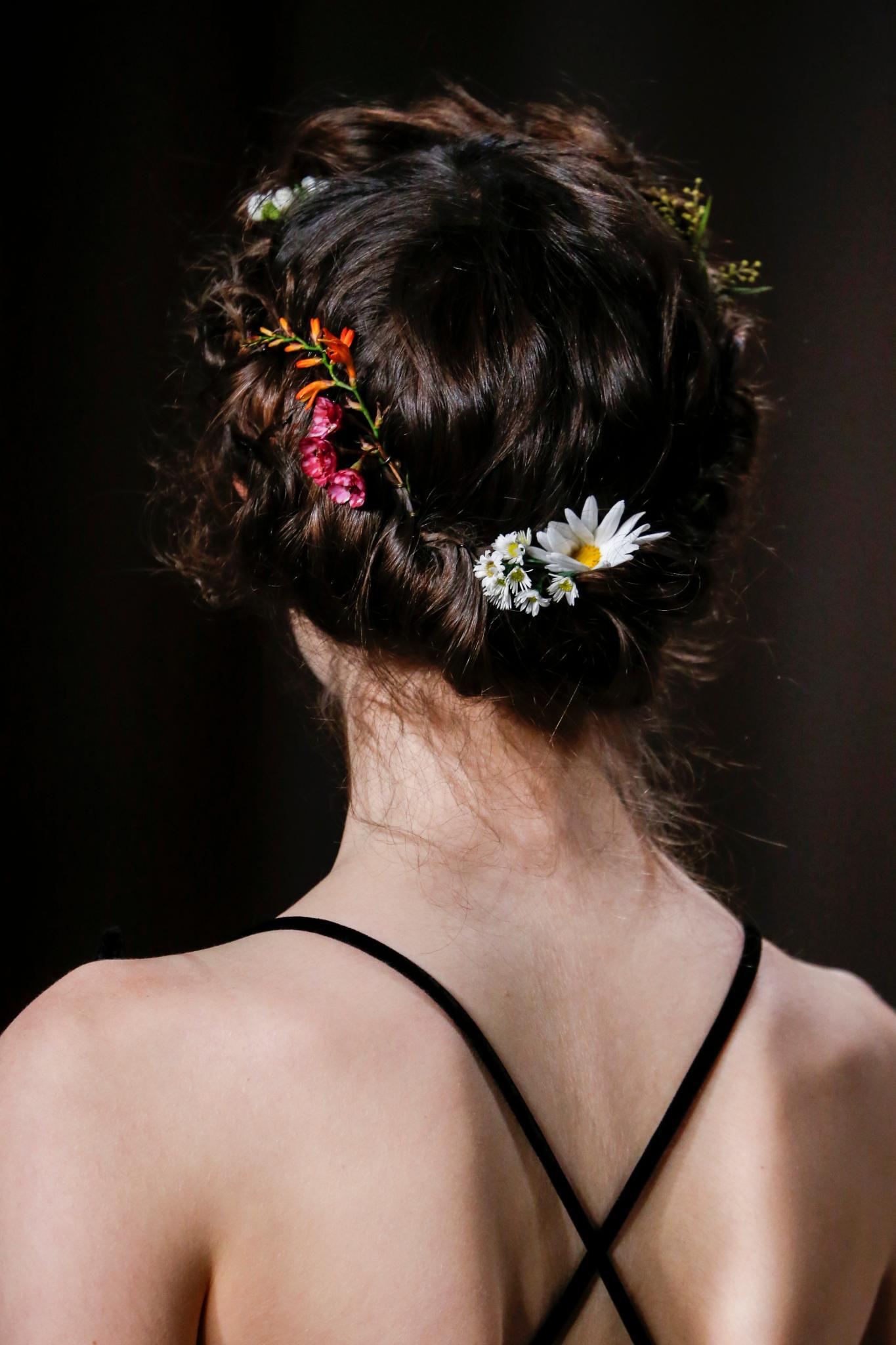 easy vintage hairstyles: close up shot of model on the valentino runway with Gibson tuck-inspired hair, with flowers in it, wearing all black