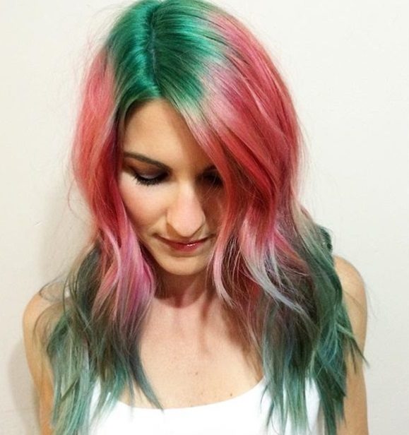 close up shot of woman with green roots, pink hair and green ends, wearing white and posing in a studio