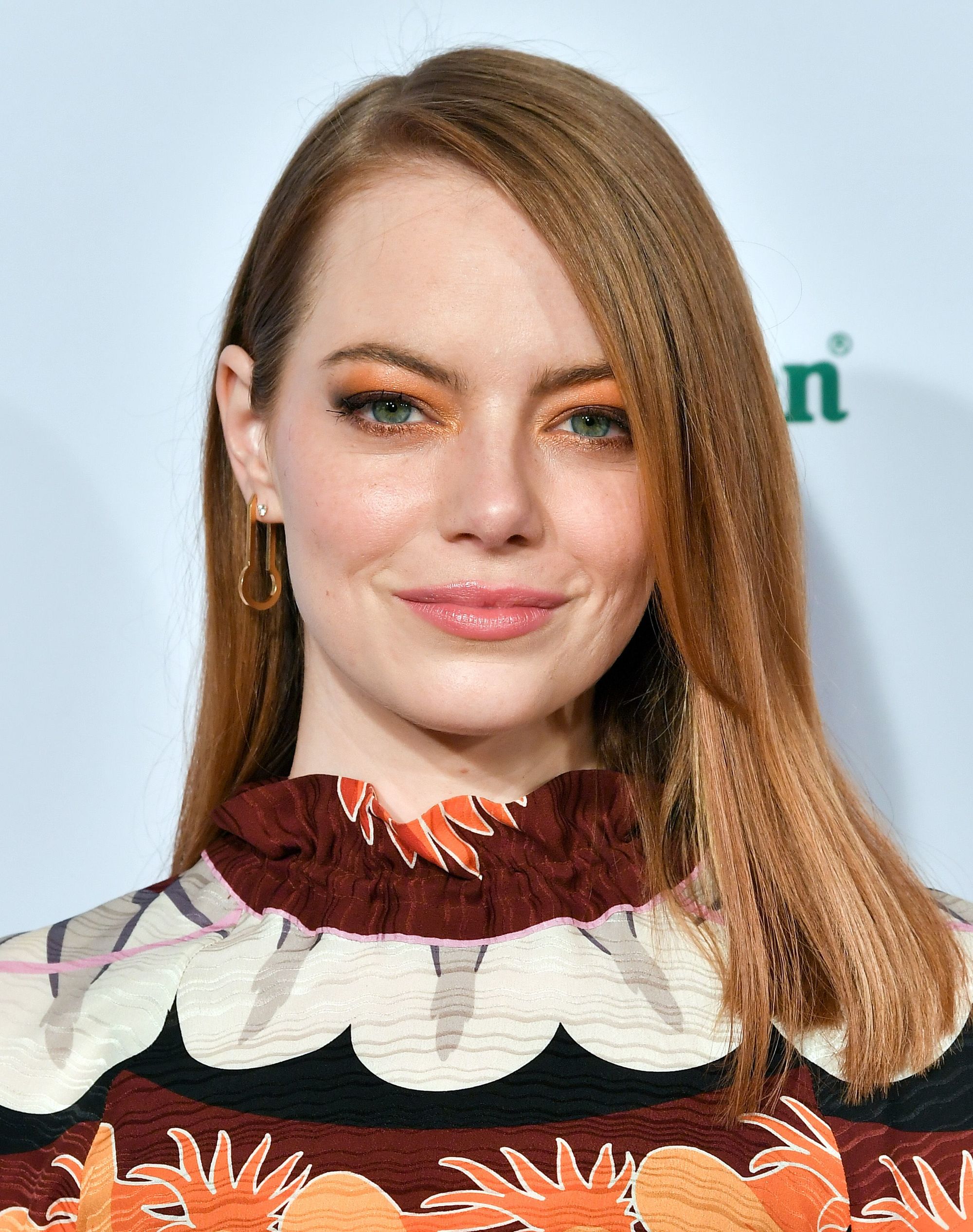 Emma stone with medium length copper hair styled to sleek and swept to the side, wearing a printed dress on the red carpet