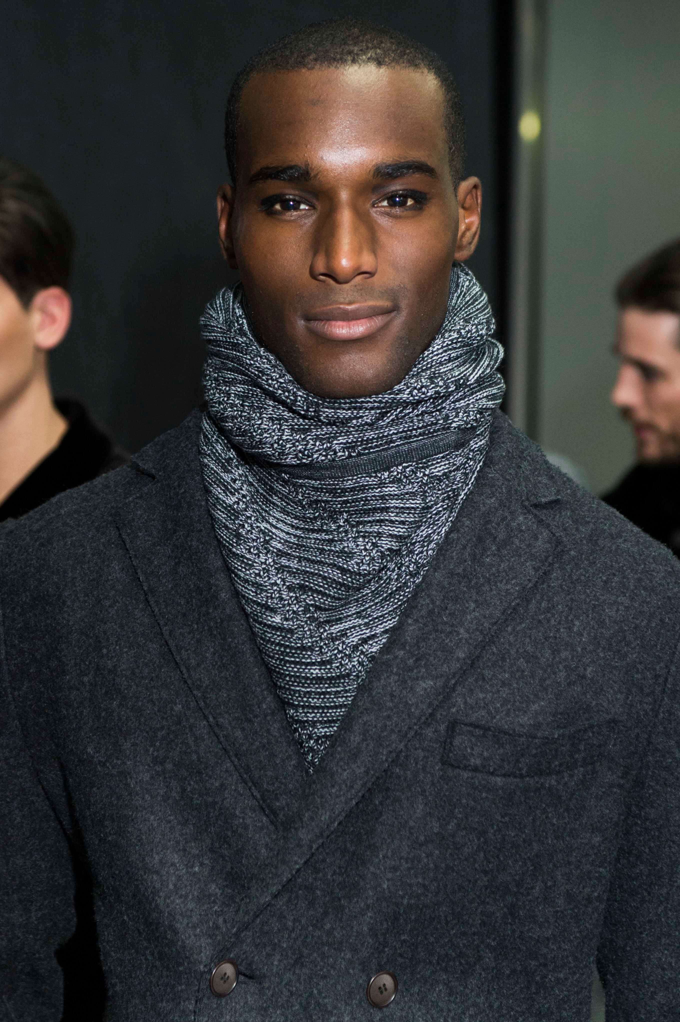 close up shot of a black male model with a buzz cut hairstyle, wearing jacket and scarf, backstage