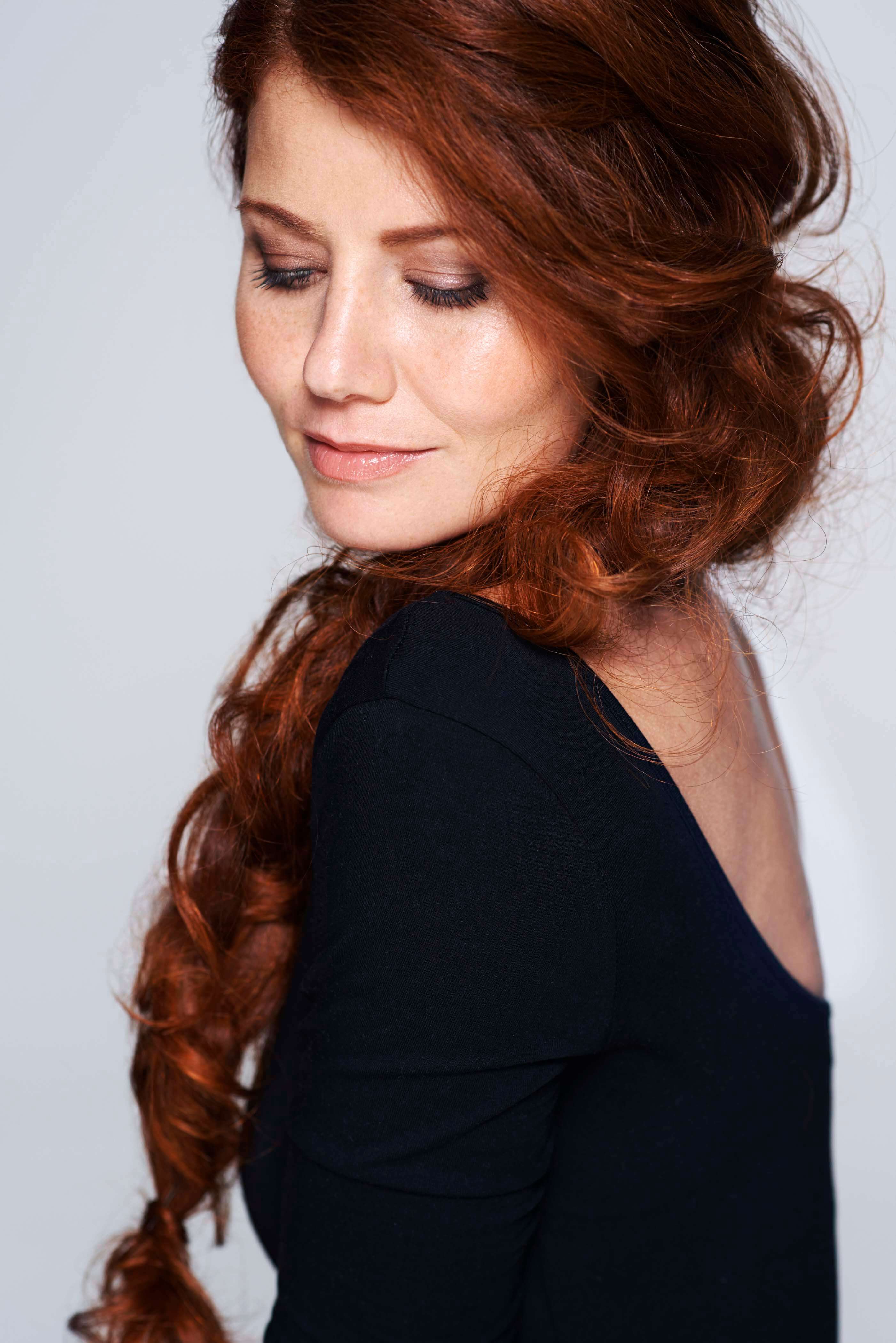 Studio shot of a young woman with beautiful red hair posing against a gray background