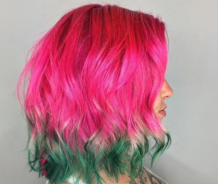 close up shot of woman with wavy neon watermelon ombre hair, posing to the side in a studio