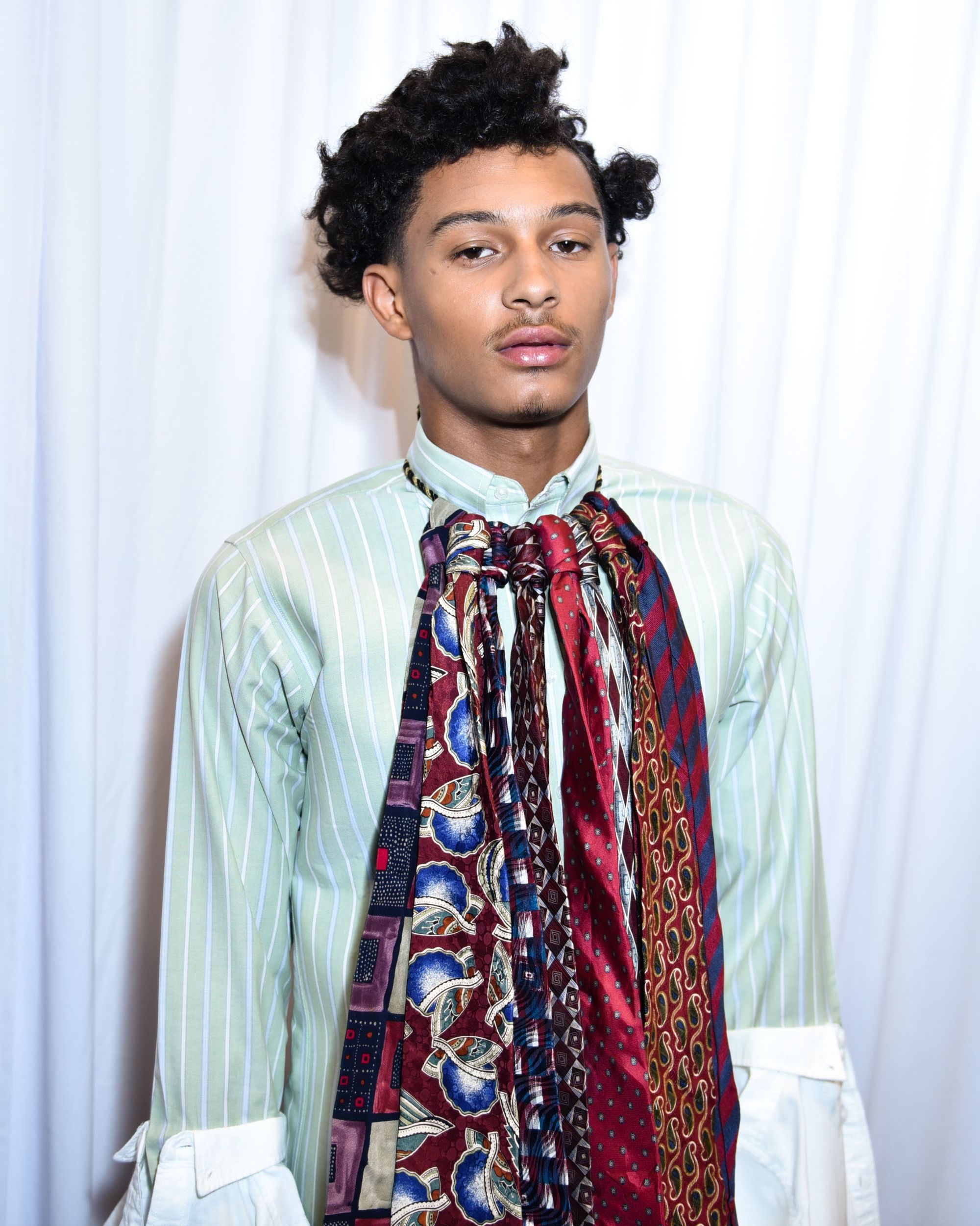 close up shot of a man with a side part afro hairstyle, backstage, wearing ties and green shirt
