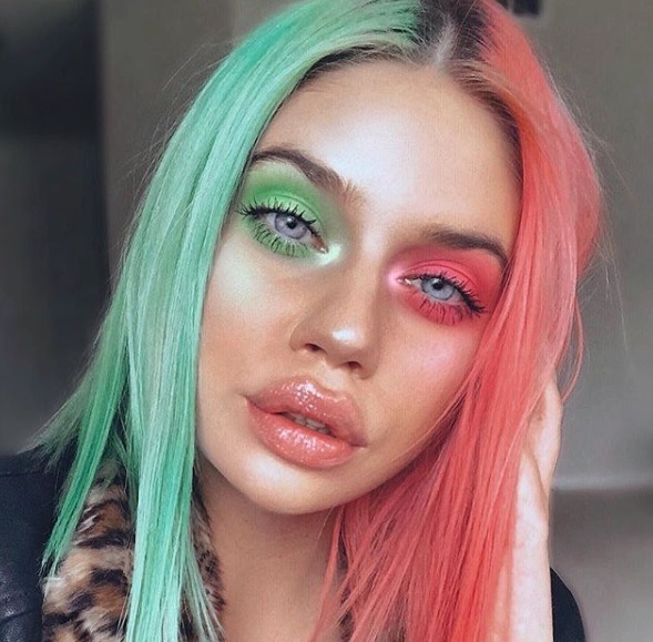 close up shot of woman with mint green and peach two-tone hair with matching make up, wearing black and posing in bedroom