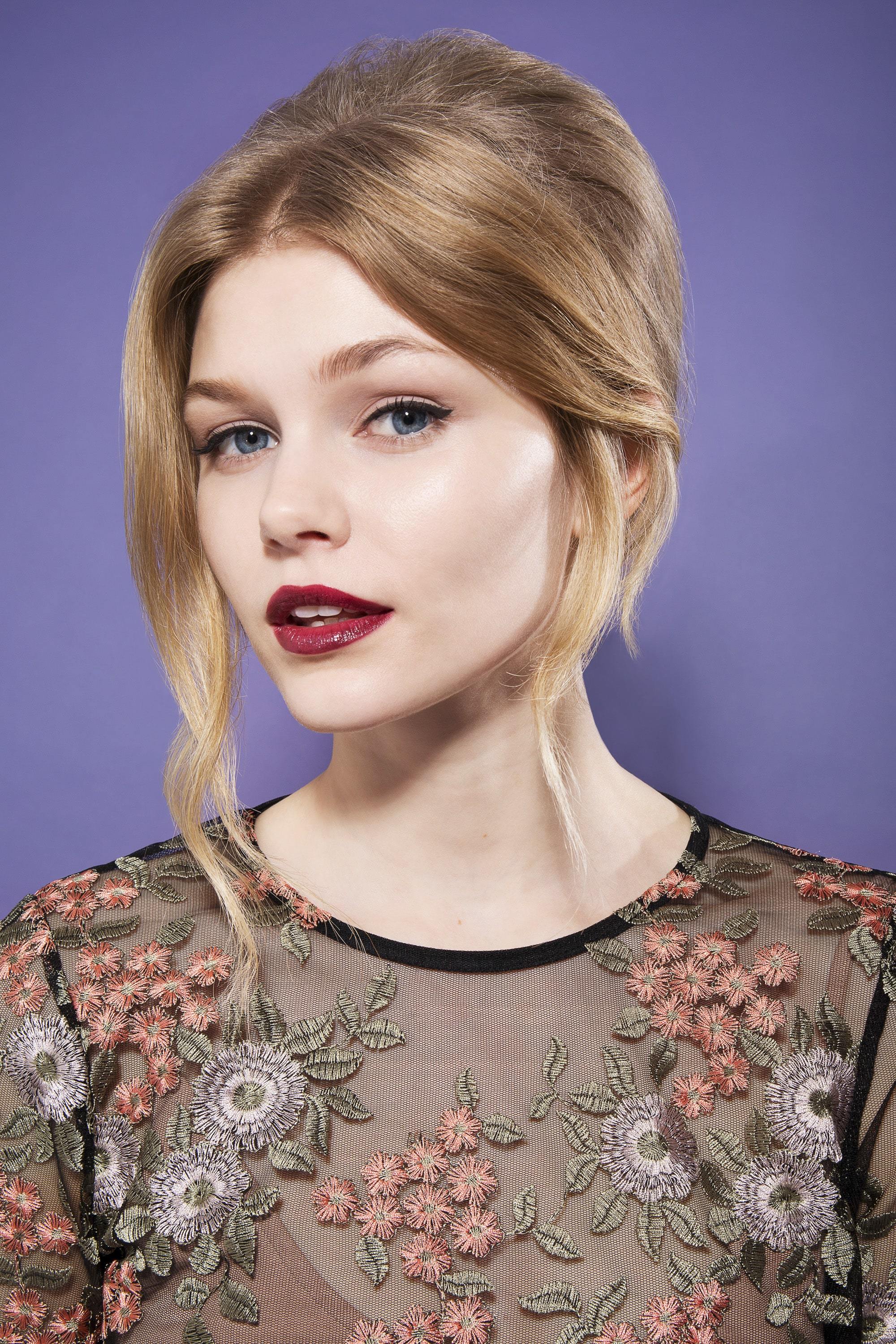 blonde model with straight and smooth hair in high beehive with loose sweeping long fringe wearing sheer floral top and dark red lipstick