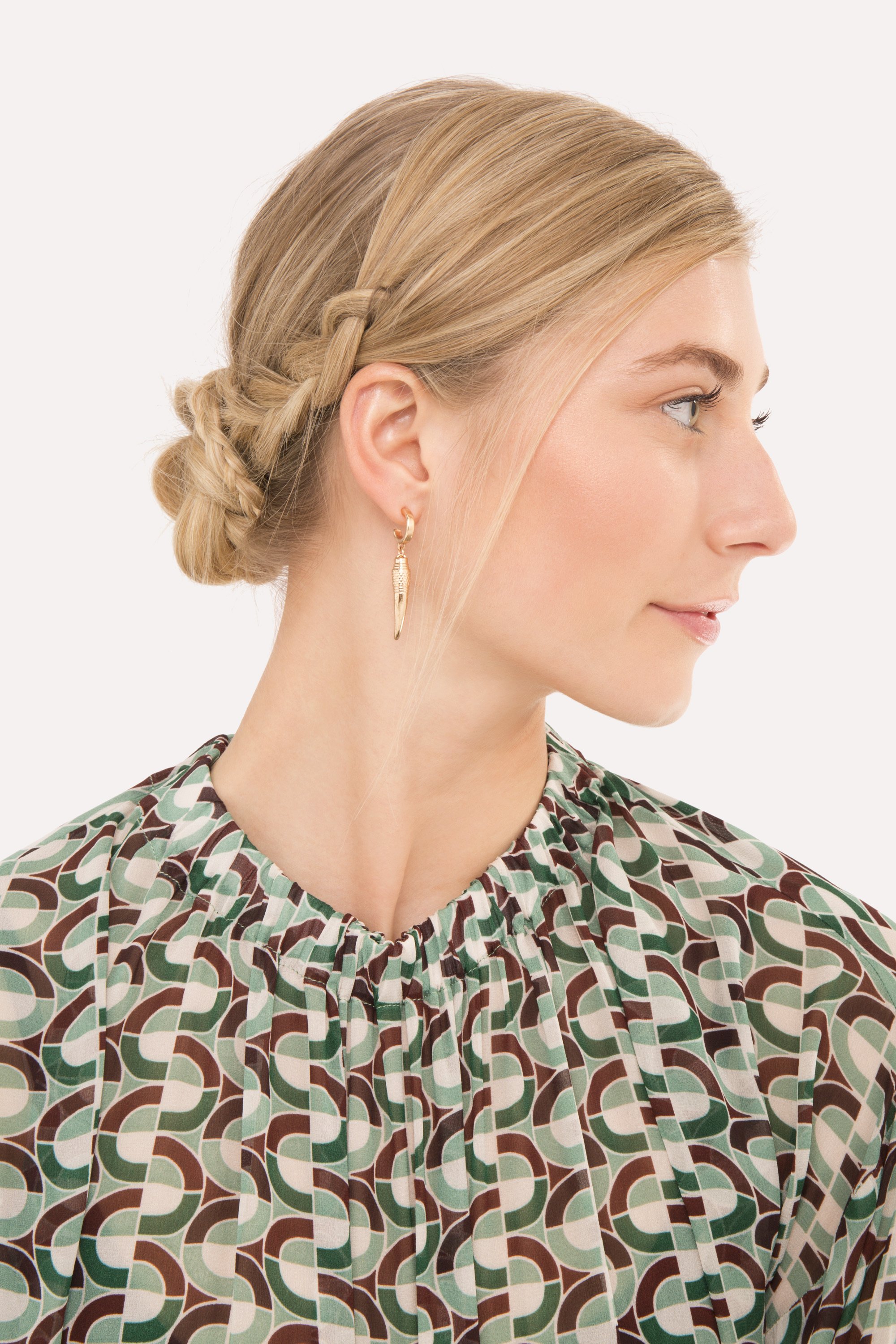 side view of model with straight blonde hair styled in a low bun with a braid detail on the side