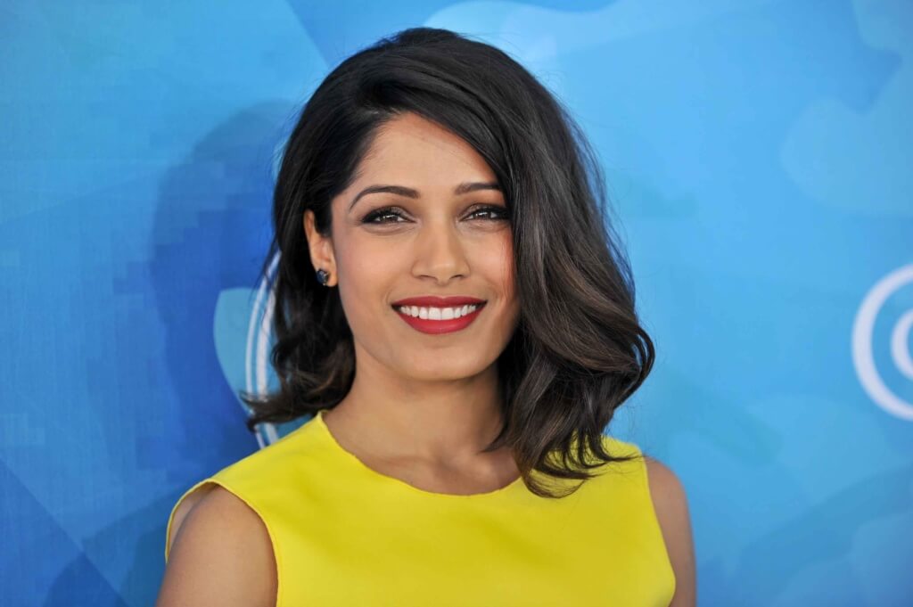 Freida Pinto with a dark brown wavy long bob wearing a yellow dress on the red carpet