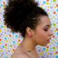 close up shot of woman with glittery afro ponytail, wearing round earrings and pink makeup