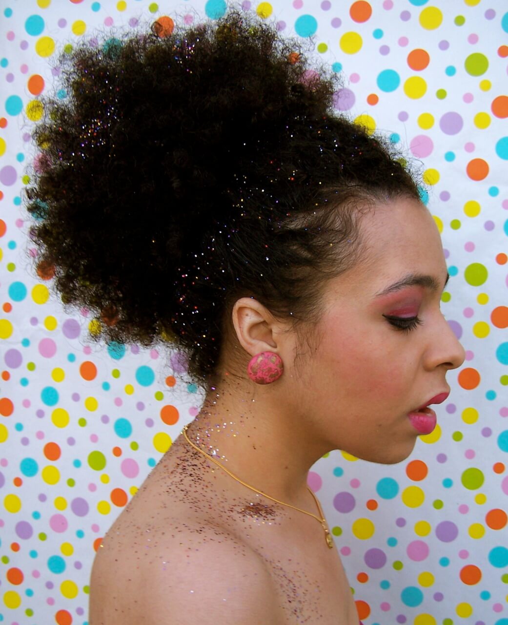 close up shot of woman with glittery afro ponytail, wearing round earrings and pink makeup