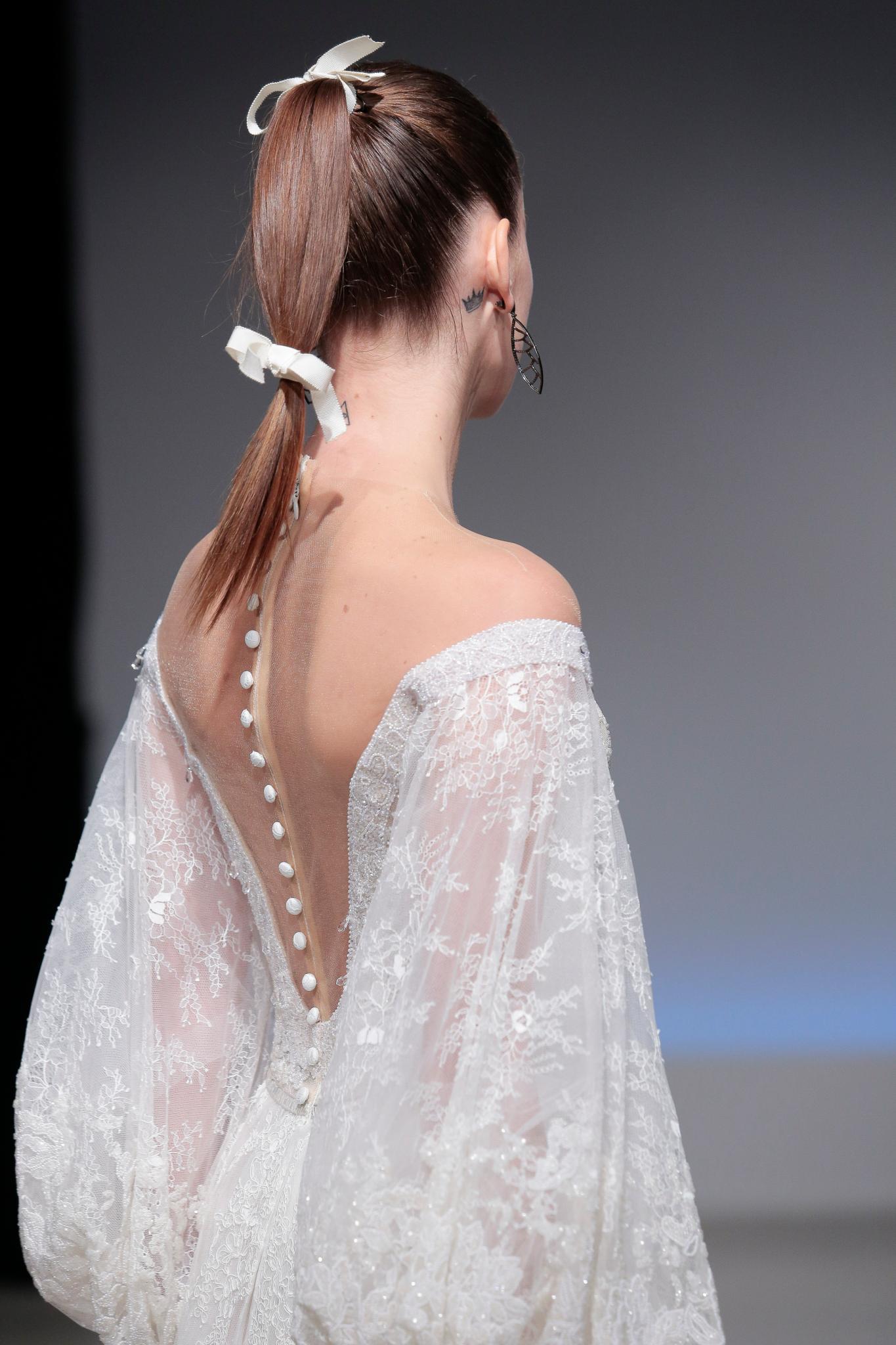 model on bridal runway with long straight dark blonde hair in high ponytail with a white bow at the base of ponytail and another half way down the length
