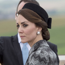 kate middleton wearing a grey outfit with her hair twisted into a low bun with a hairnet accessory and a black hat