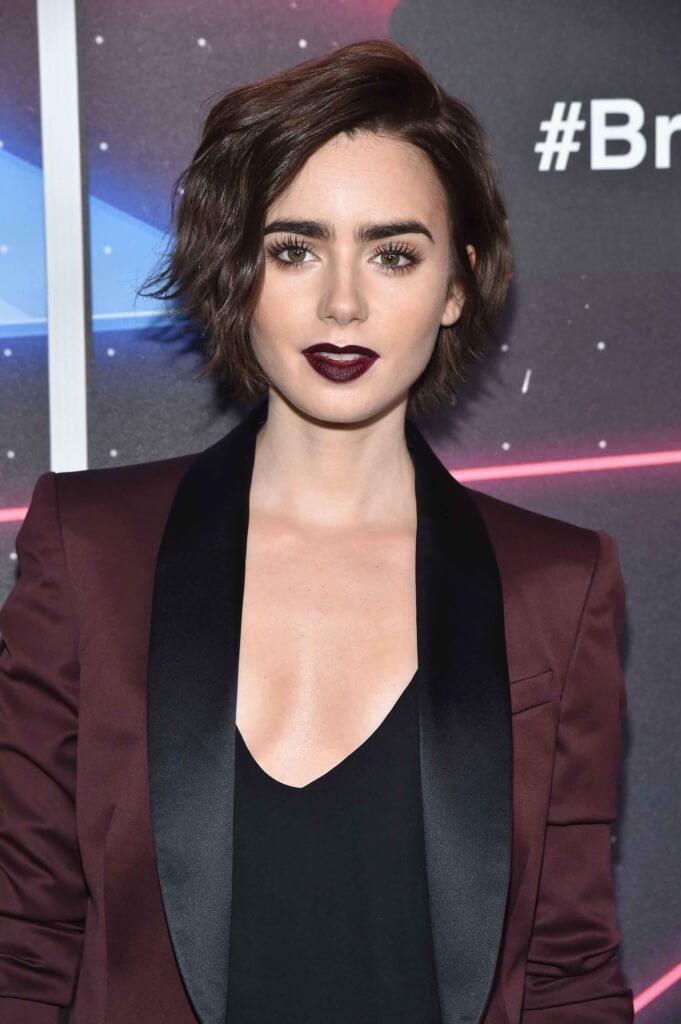lily collins with a dark brown wavy bob in side parting wearing a burgundy blazer