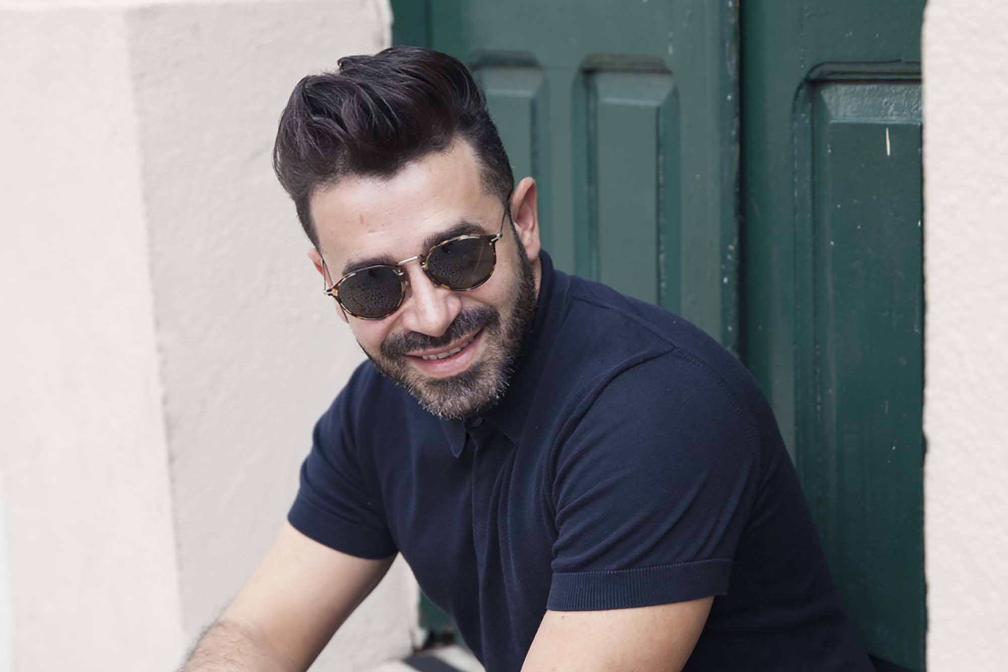 Best hair styling products for men: Close up shot of a man with dark brown hair styled into a pompadour, wearing blue and posing out