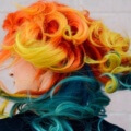side view of a woman swishing her curly hair, coloured orange and yellow at the top and a mix of blues at the bottom