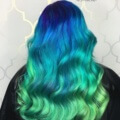 back view of a woman with long wavy hair in an ombre style, starting with dark blue at the top and flowing into light, seafoam green at the tips