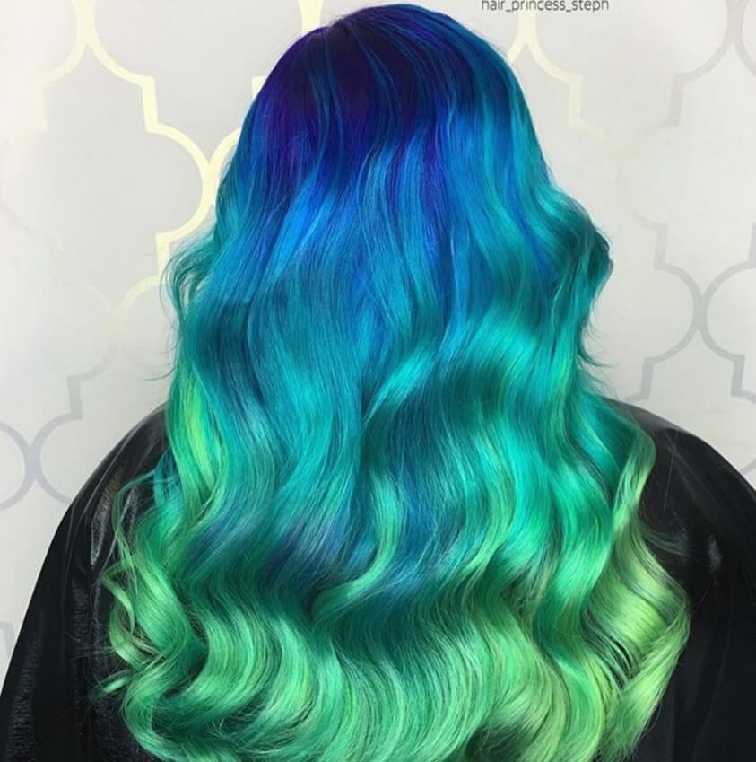 back view of a woman with long wavy hair in an ombre style, starting with dark blue at the top and flowing into light, seafoam green at the tips