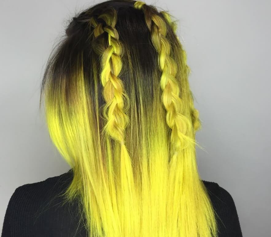 back view of a woman with bright yellow ombre hair with dark roots and two braids