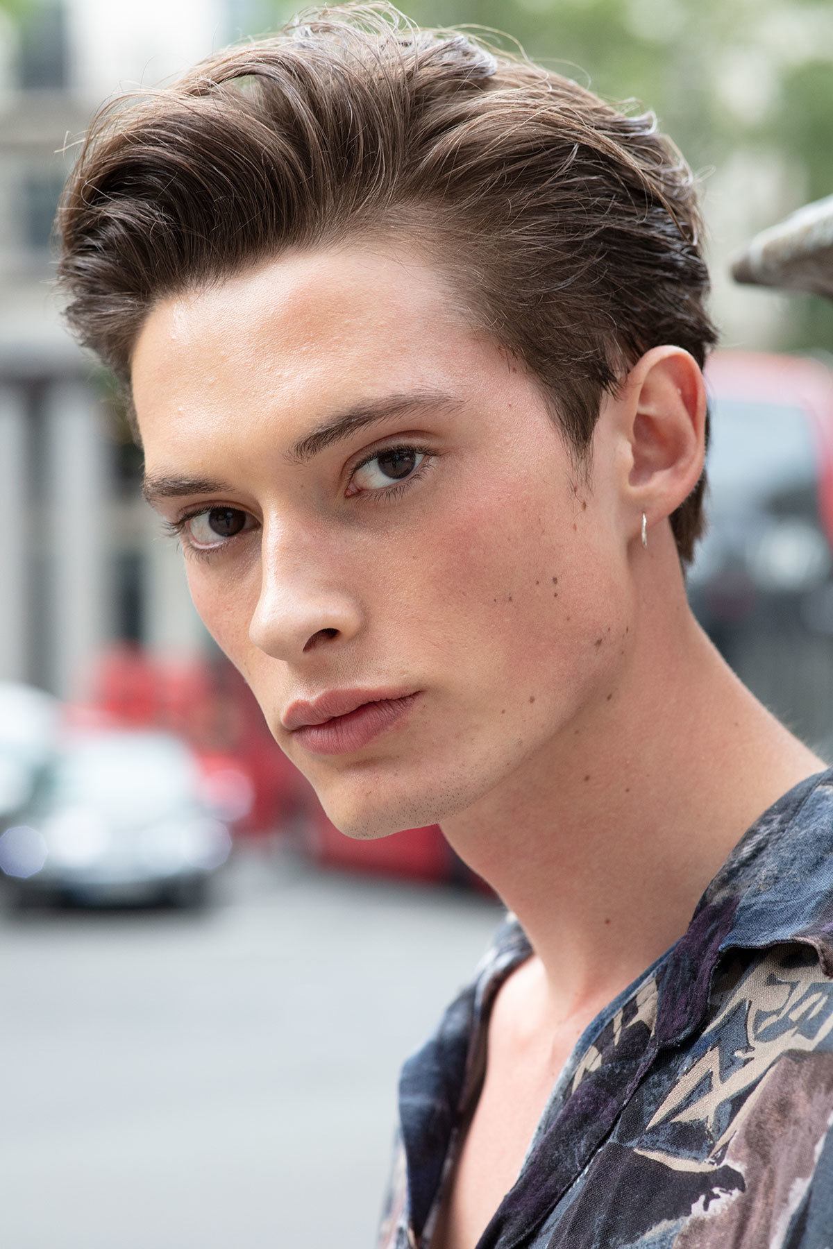 Best hair styling products: Close up shot of a man with medium brown hair styled into a relaxed quiff, wearing printed top and posing on the street.